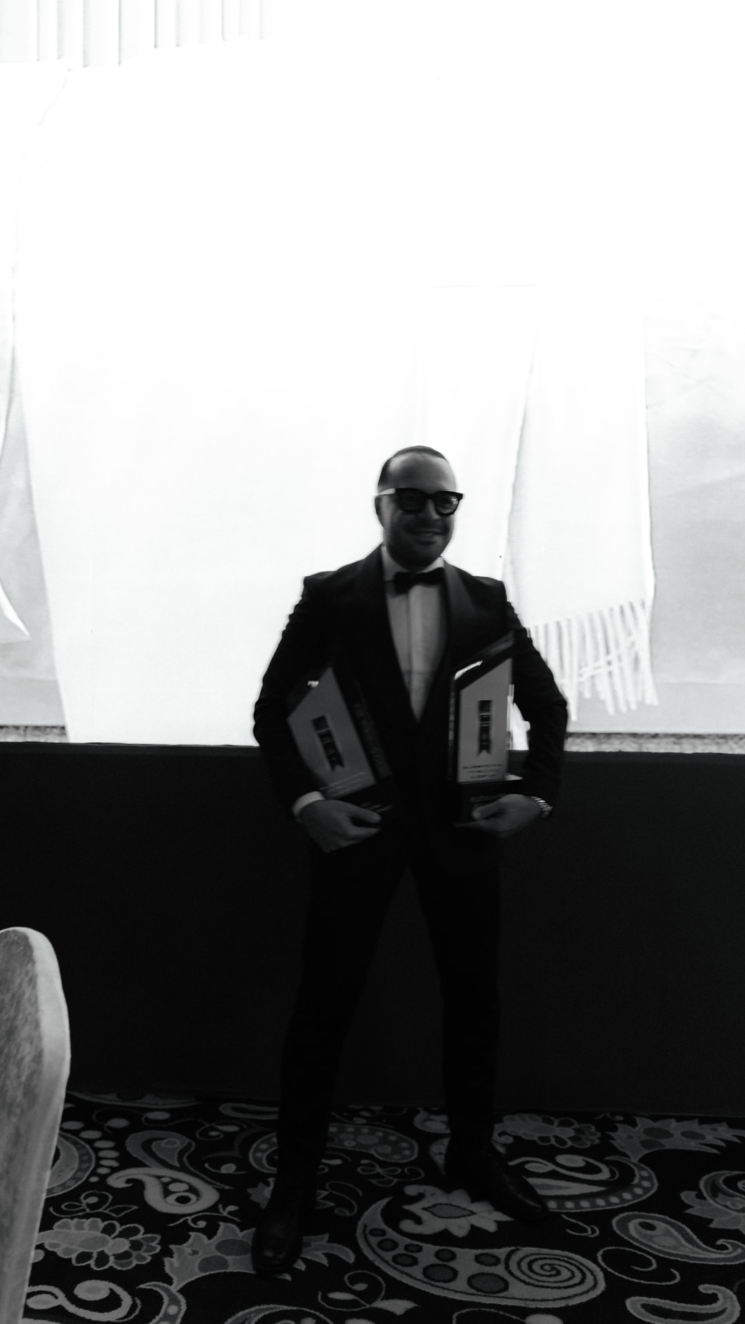 Kaveh Jafari in a tuxedo holding two industry awards